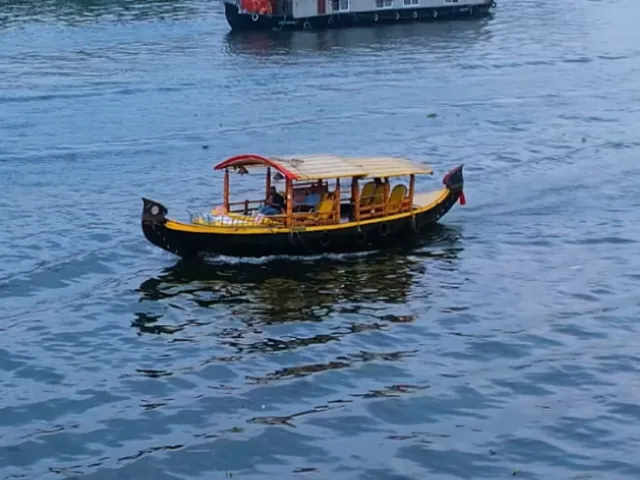 A shikara crossing the backwaters, a houseboat behind it