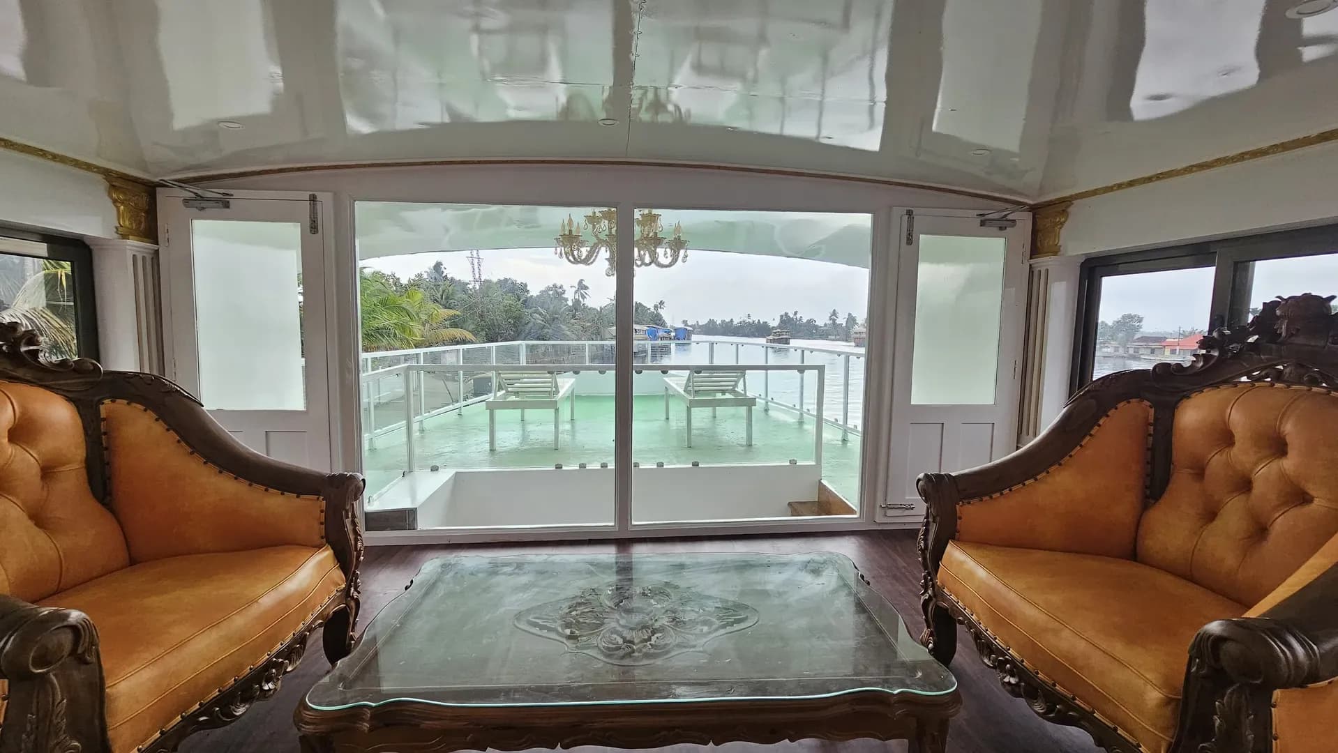 Air-conditioned houseboat lounge with the Alleppey backwaters and coconut palms visible through the glass front