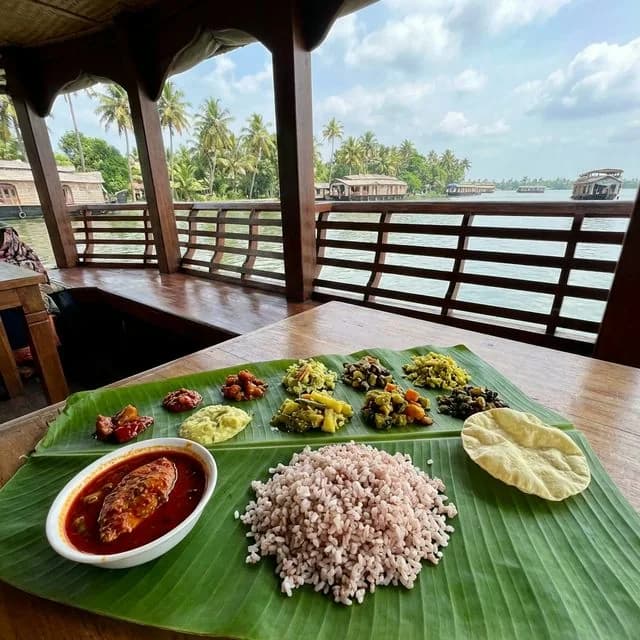 Kerala lunch of matta rice, fish curry, thoran and papad served on a banana leaf at a houseboat dining table overlooking the Alleppey backwaters